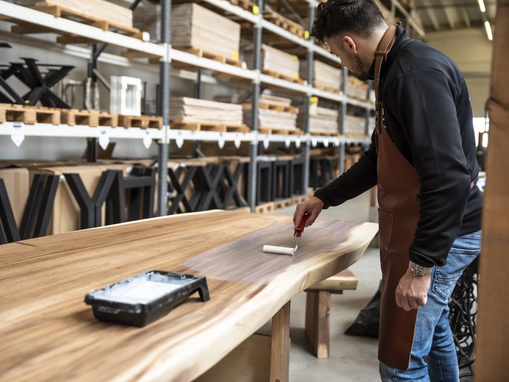 een houten tafelblad behandelen met een 2-componentenlak door een medewerker van Bouwie