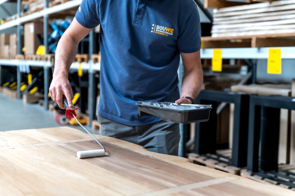 een houten tafelblad behandelen met een 2-componentenlak door een medewerker van Bouwie