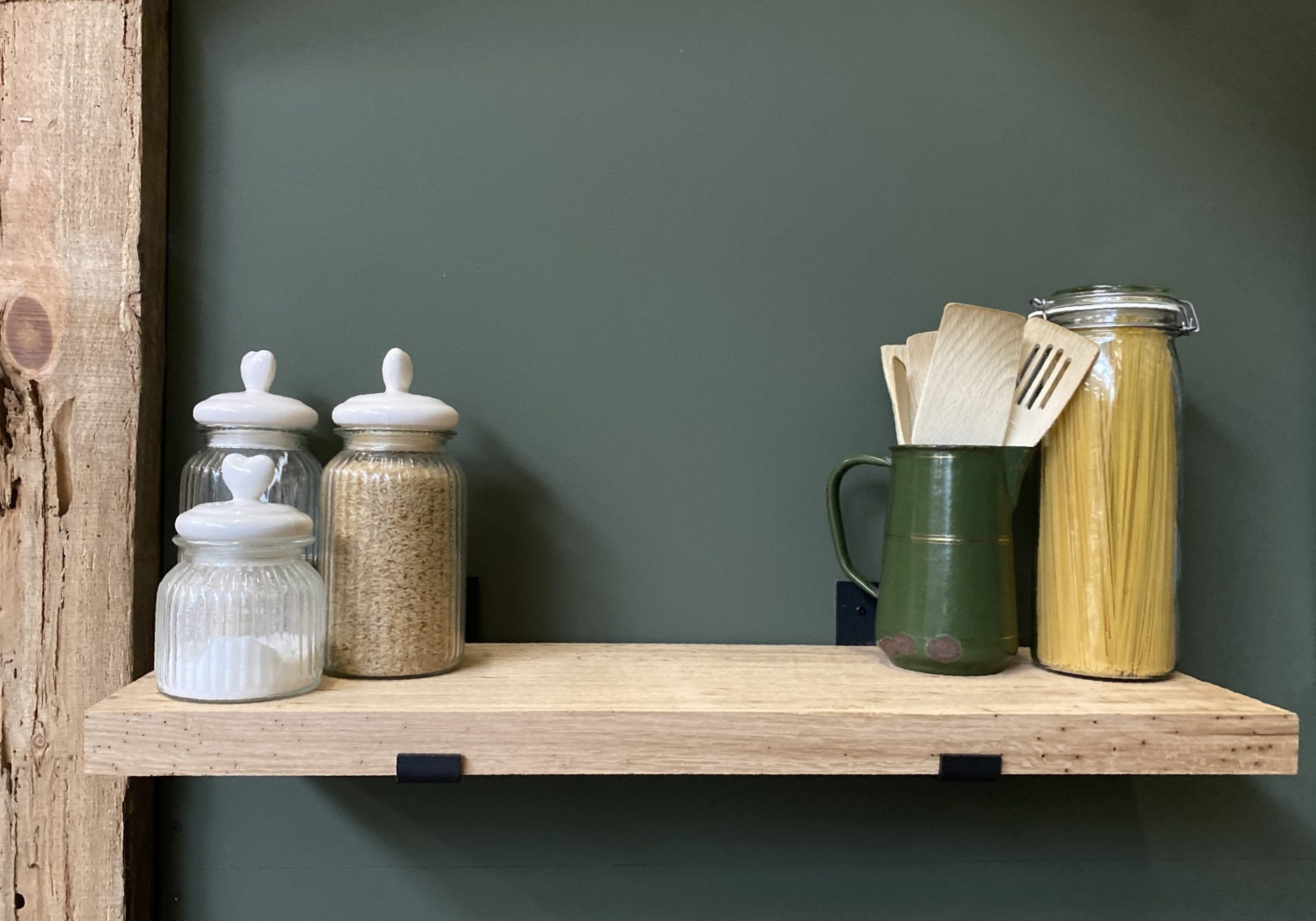 Eiken wandplank van massief oud eiken, gehangen aan zwarte plankdragers tegen een groene wand. op de wandplank staan enkele decoratieve potjes. Deze eiken wandplank van oud eiken koop je bij Bouwie in Veen